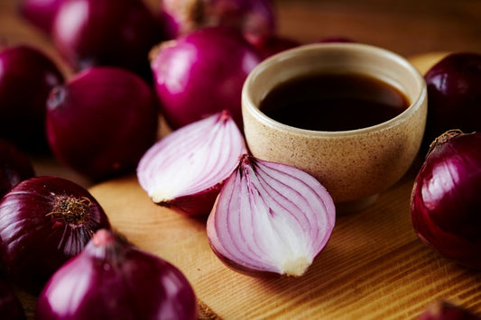 Eine Schale Zwiebelsaft inmitten von mehreren roten Zwiebeln